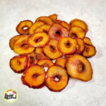 اسلایس‌های حلقه‌ای آلو شابلون خشک با پوست قرمز و گوشت زرد رنگ که روی سطحی سفید چیده شده‌اند.