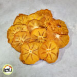 اسلایس‌های خرمالو خشک ممتاز با رنگ نارنجی طلایی و طرح ستاره‌ای در مرکز که روی سطحی روشن قرار گرفته‌اند.