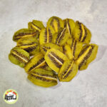 اسلایس‌های طولی کیوی خشک با رنگ سبز روشن و دانه‌های سیاه که روی سطحی خاکستری قرار گرفته‌اند.