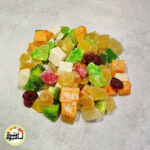 انبوهی از مخلوط حبه‌های استوایی (۶ میوه) با رنگ‌های متنوع سفید، زرد، نارنجی، قرمز و سبز که روی سطحی خاکستری و روشن قرار گرفته‌اند.