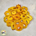 اسلایس‌های حلقه‌ای زردآلو خشک با رنگ نارنجی روشن و جذاب که روی سطحی روشن چیده شده‌اند.
