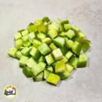 انبوهی از تکه‌های مکعبی و سبز رنگ پوملو حبه‌ای که روی سطحی خاکستری و روشن قرار گرفته‌اند.