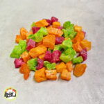 انبوهی از تکه‌های مکعبی و رنگارنگ آناناس حبه‌ای با رنگ‌های سبز، نارنجی و قرمز که روی سطحی خاکستری و روشن قرار گرفته‌اند.