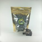 بسته بندی شفاف و طلایی آسان میوه خشک حاوی حبه‌های کیوی، با چند تکه مکعبی و تیره رنگ در جلوی آن.