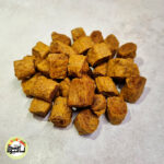 انبوهی از تکه‌های مکعبی و قهوه‌ای-طلایی حبه زردآلو فشرده که روی سطحی خاکستری و روشن قرار گرفته‌اند.