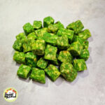 انبوهی از تکه‌های مکعبی و سبز رنگ حبه سیب ترش فشرده که روی سطحی خاکستری و روشن قرار گرفته‌اند.