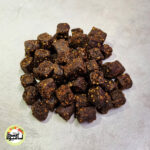 انبوهی از تکه‌های مکعبی و تیره رنگ حبه انجیر فشرده که روی سطحی خاکستری و روشن قرار گرفته‌اند.