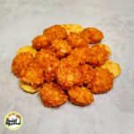 انبوهی از چیپس میگو (اسنک برنجی) با رنگ نارنجی و بافت پفکی که روی سطحی خاکستری قرار گرفته‌اند.