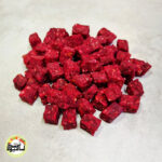 انبوهی از تکه‌های مکعبی و سرخ رنگ حبه سیب لبویی که روی سطحی خاکستری و روشن قرار گرفته‌اند.