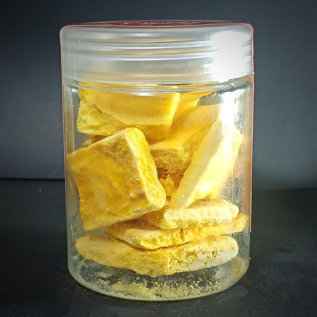 اسلایس‌های انبه خشک انجمادی با رنگ زرد روشن و بافت پفکی در یک ظرف شیشه‌ای شفاف.