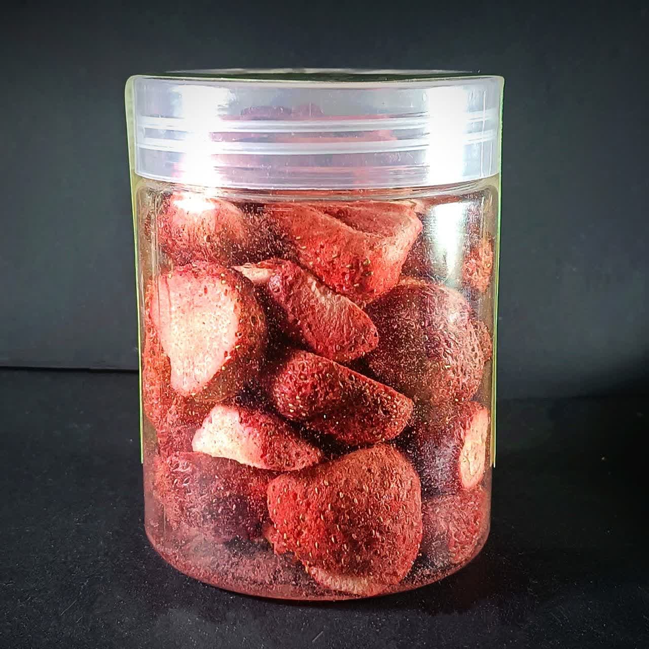 توت فرنگی‌های خشک انجمادی درسته با رنگ قرمز روشن در یک ظرف شیشه‌ای شفاف.