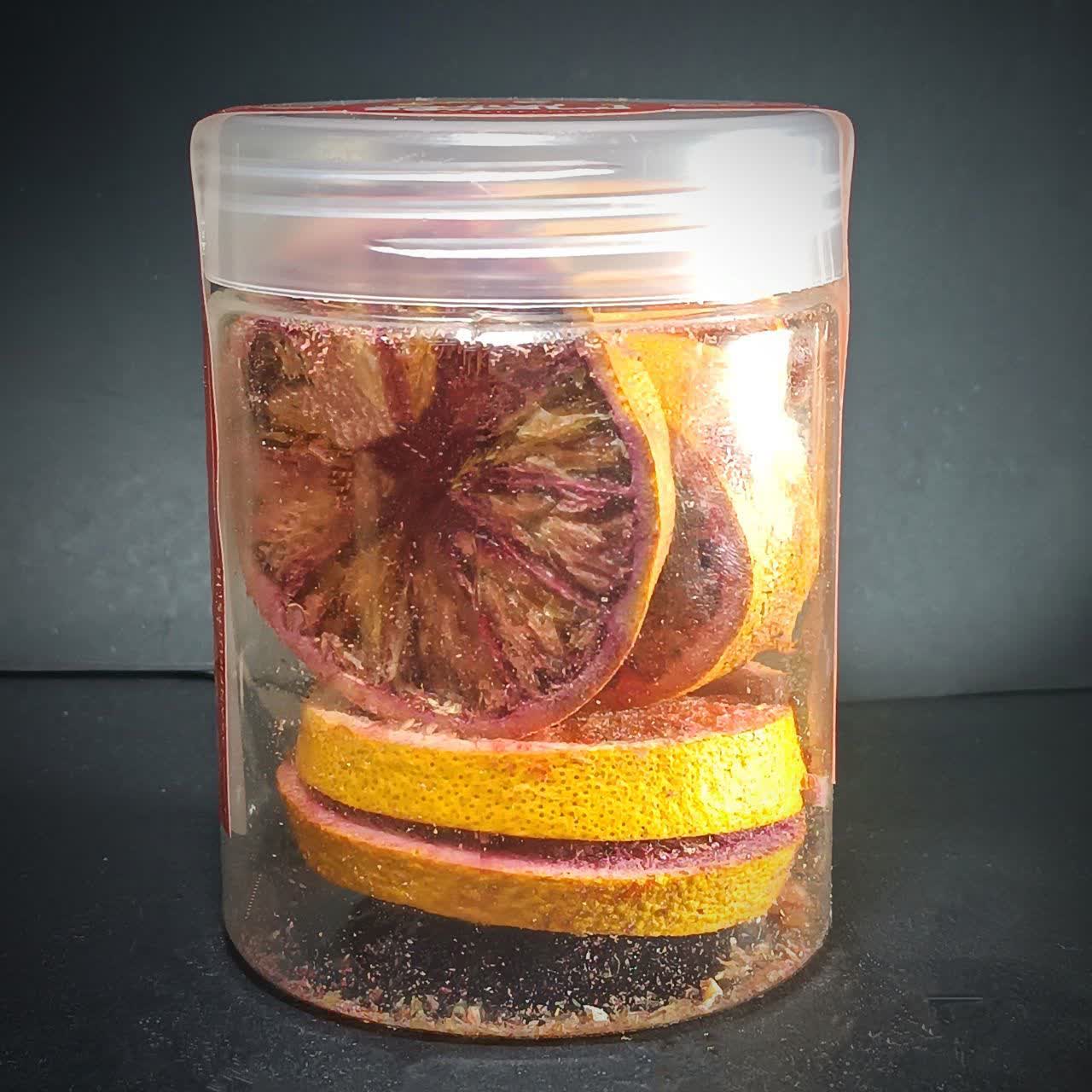 اسلایس‌های پرتقال تو سرخ خشک انجمادی با رنگ‌های نارنجی و قرمز خونی در یک ظرف شیشه‌ای شفاف.